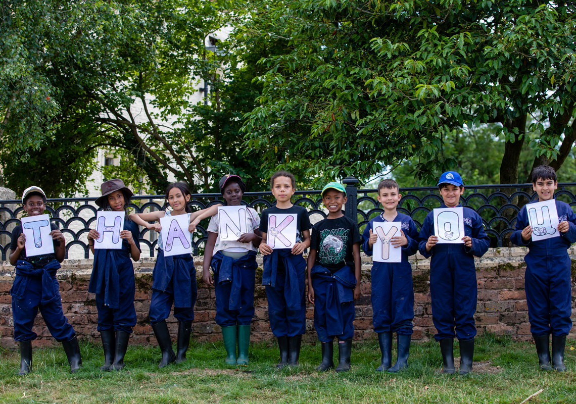 Line of children in Farms for City Children overalls with cards spelling thank you