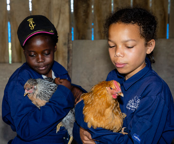 Two girls wearing overalls holding chickens